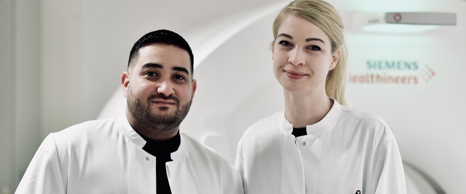 Zwei Mitarbeitende vor einem CT in der Arbeitskleidung in der Röntgenabteilung